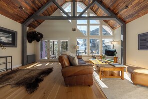 A spacious living room with a large brown leather sofa, wooden coffee table, and a fur rug.