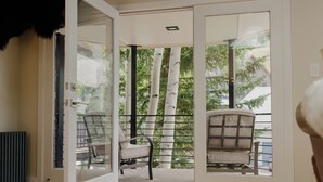 Une porte-fenêtre coulissante s’ouvre sur un balcon équipé de deux chaises et offrant une vue sur des bouleaux.