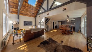 Un vaste espace de vie doté d’un haut plafond, de poutres en bois, d’une grande fenêtre, d’une cheminée, d’un canapé, d’une table à manger et d’un tapis en fourrure.