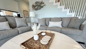 A modern living room with a grey sofa set, a round coffee table with a woven tray, and a decorative wall piece.