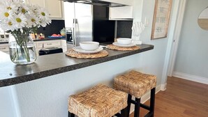 A kitchen island with two woven stools, a vase of white flowers, and a set of white bowls on woven placemats.