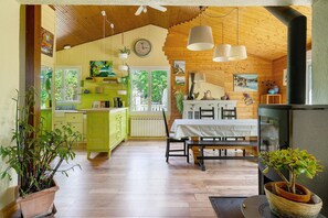 A cozy interior with wooden beams, a dining area, a kitchen, and a large window.