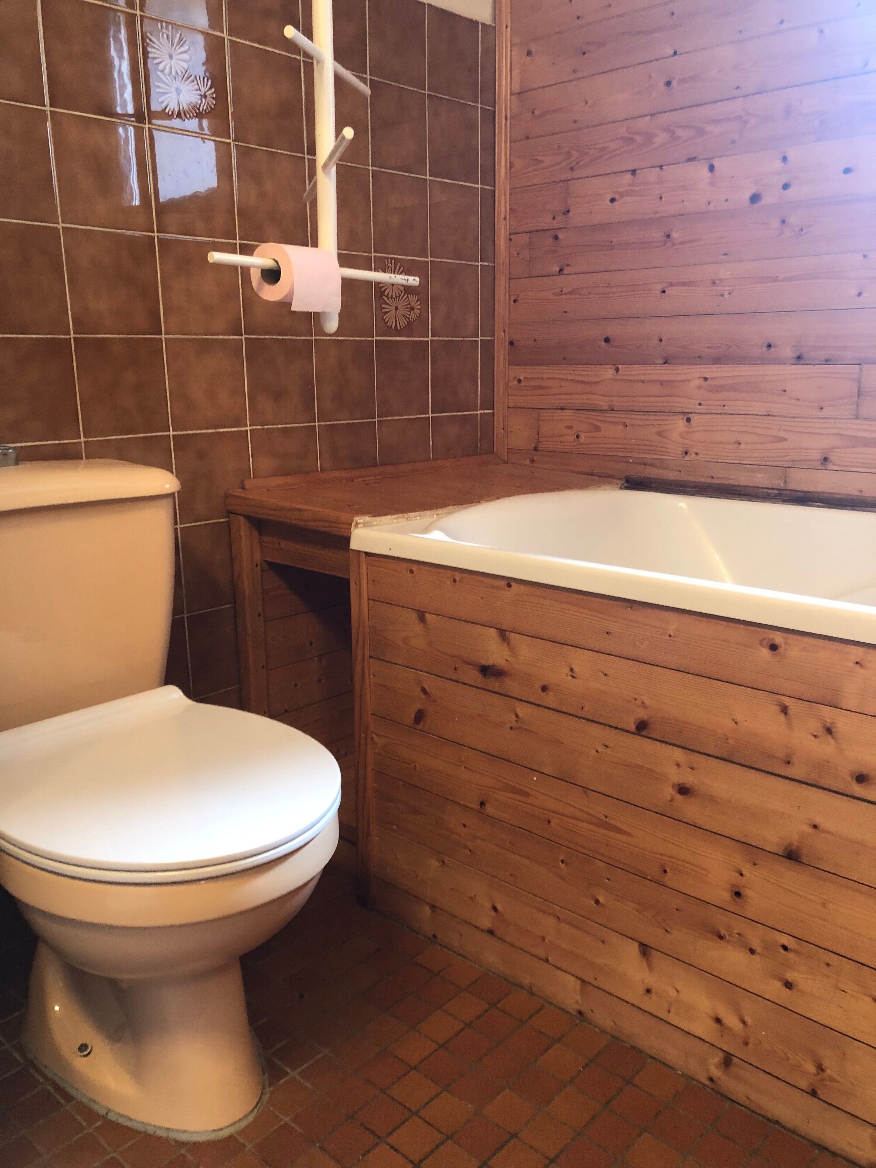Een badkamer met een toilet, een houten badkuip en betegelde wanden.