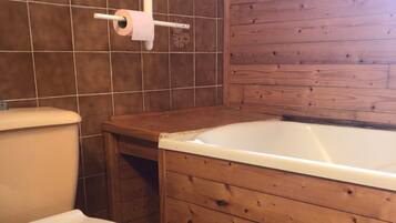 Een badkamer met een toilet, een houten badkuip en betegelde wanden.