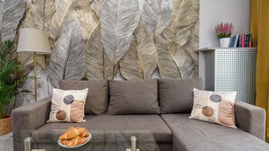 A modern living room with a grey sofa, patterned cushions, a glass coffee table, and a decorative wall.