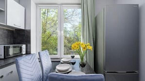 A modern kitchen with a large window, a refrigerator, a microwave, and a dining area with chairs and a table set for two.
