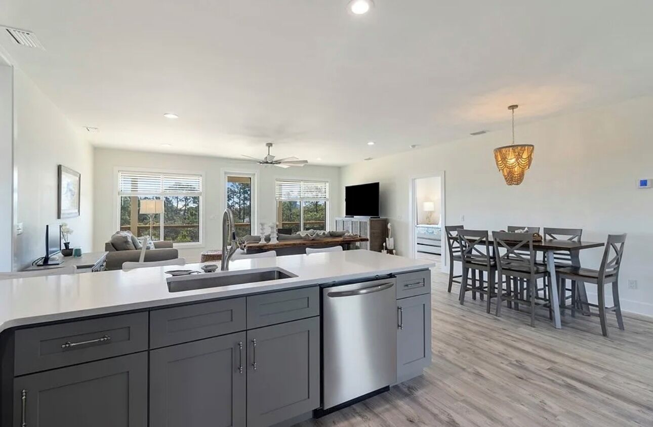 Una cocina moderna con una isla grande, un comedor con sillas de madera y un ventilador de techo.
