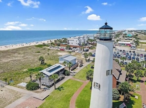 A coastal view with a lighthouse, beach, parking area, and buildings.