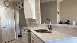 A kitchen with white cabinets, a double sink, and a herringbone tile backsplash. - Waterfront Playground in Paradise - more than a condo rental, a destination! (Destin)