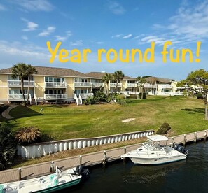A waterfront hotel with multiple balconies, a grassy lawn, and boats docked at the pier.