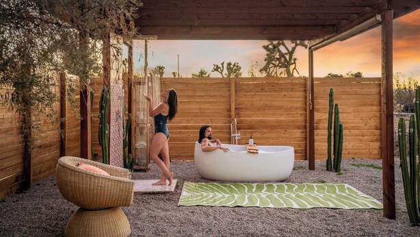 Une pergola en bois avec une baignoire blanche et un fauteuil en osier.