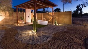 Un espace extérieur abrité, doté d’une pergola en bois, d’un évier extérieur blanc et de quelques cactus.