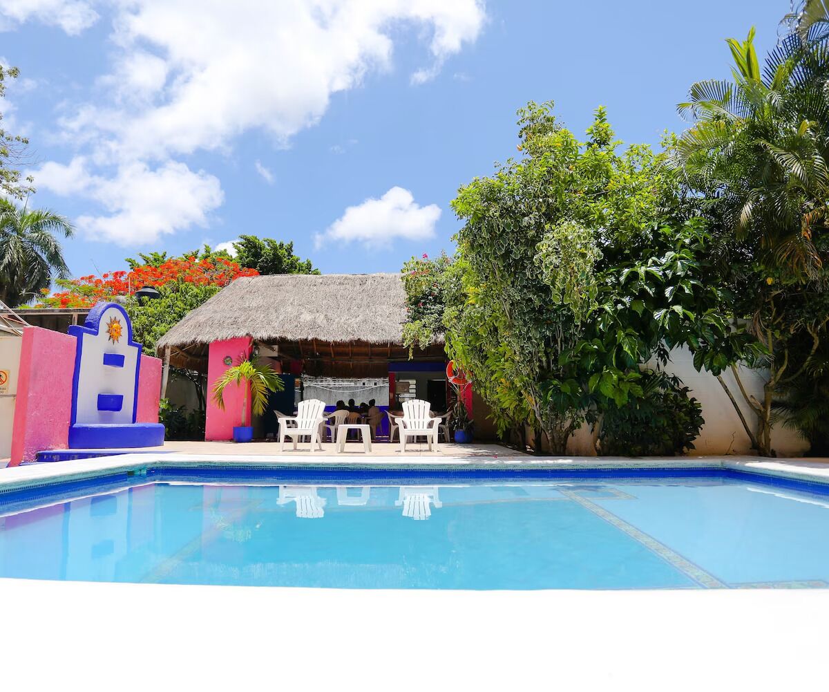 A swimming pool with a thatched-roof structure and white chairs in the background.