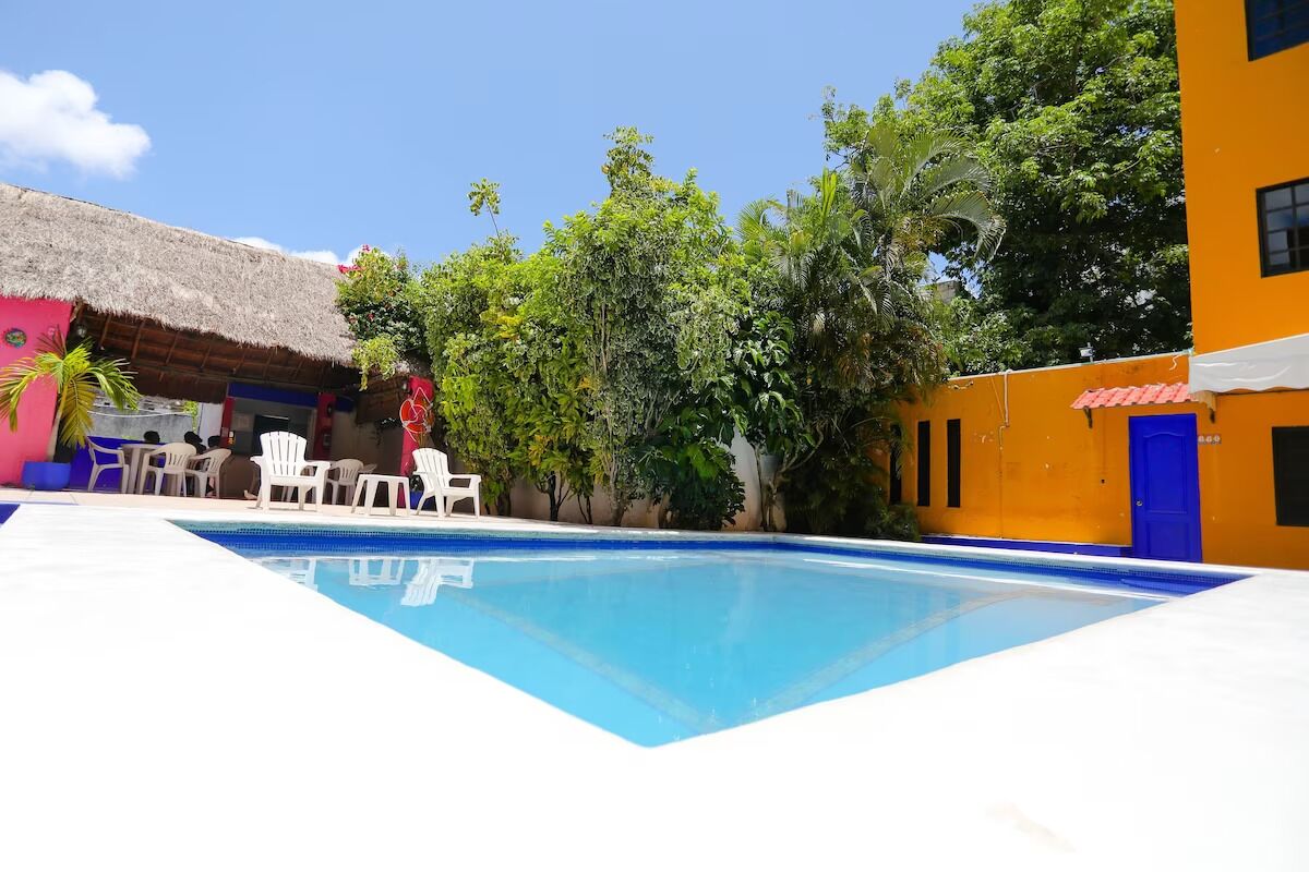 Une piscine entourée de chaises blanches, une structure à toit de chaume et une végétation luxuriante.