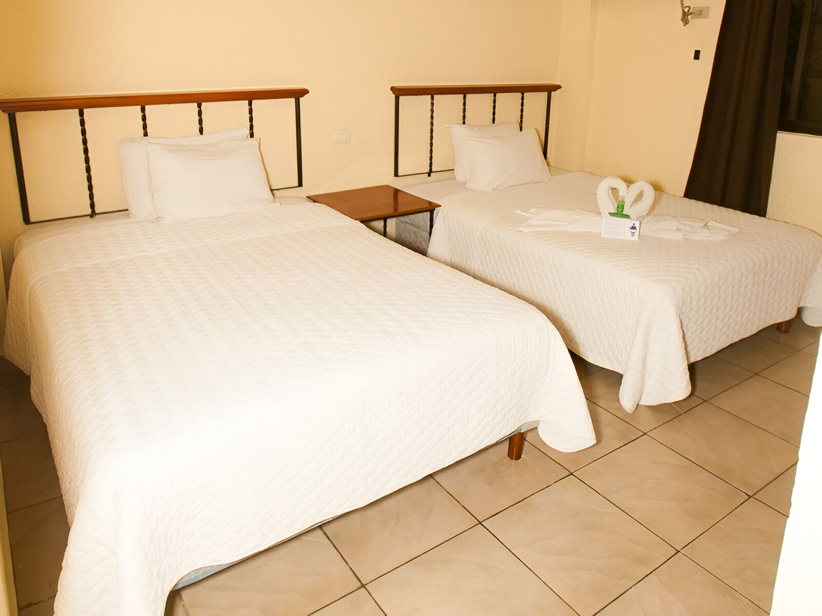 Une chambre d’hôtel avec deux lits simples, chacun doté d’une tête de lit en bois, de draps blancs et d’une petite table de chevet.