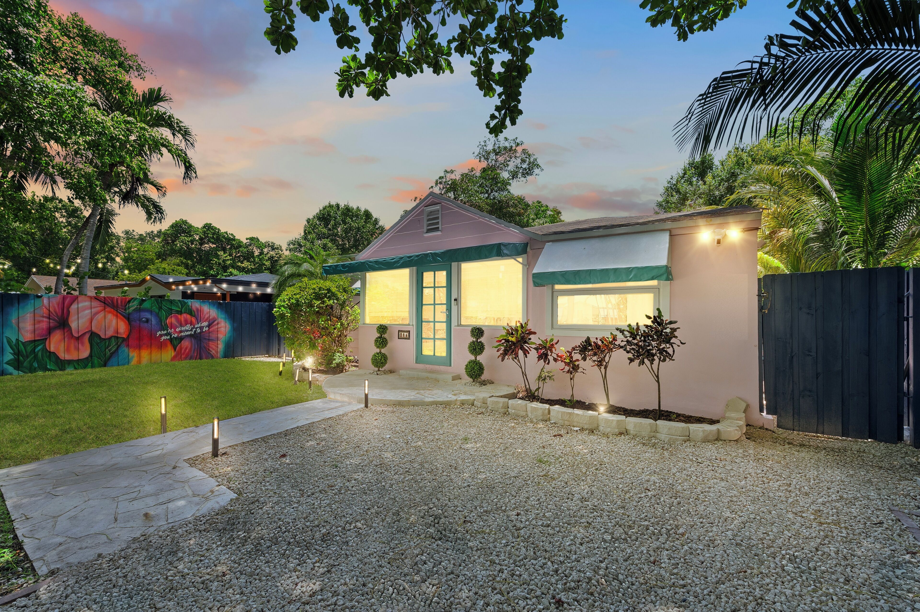 A modern house with a well-maintained lawn, a gravel driveway, and a colorful mural on the wall.