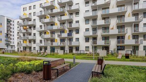 A modern apartment building with balconies, a paved walkway, and green landscaping.