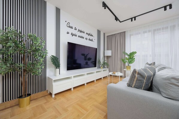 Una sala de estar moderna con un televisor de pantalla plana, un mueble bajo blanco y un sofá gris.