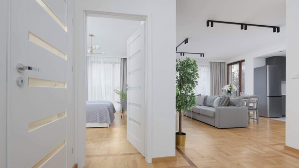 A modern apartment with a wooden floor, a grey sofa, a dining area, and a kitchen.