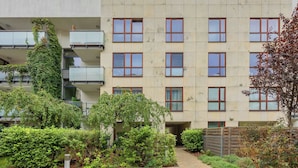 A multi-story building with a garden courtyard, featuring a pathway, various plants, and a metal fence.
