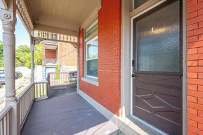 A porch with a wooden deck, a red brick wall, and a brown door.