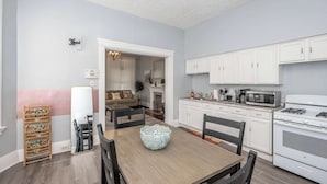 Un coin repas avec une table en bois, des chaises et un bol décoratif. La cuisine est équipée de meubles blancs et d’un four à micro-ondes.