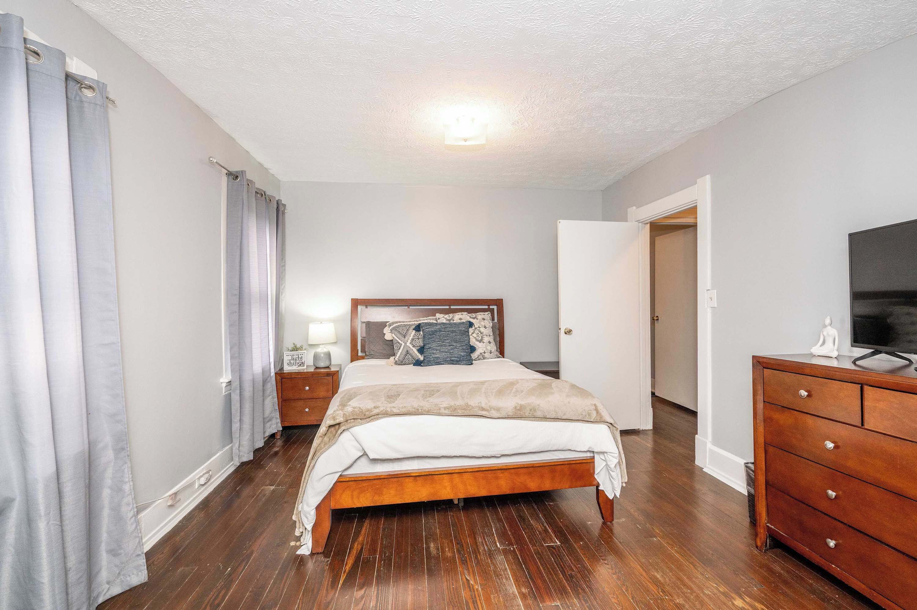 A bedroom with a wooden bed, a dresser, a TV, and a nightstand with a lamp.