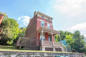 A two-story brick building with a porch and a stone wall in front.