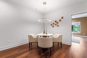A dining area with a round table, four chairs, a modern pendant light, and a wall with decorative wooden elements.