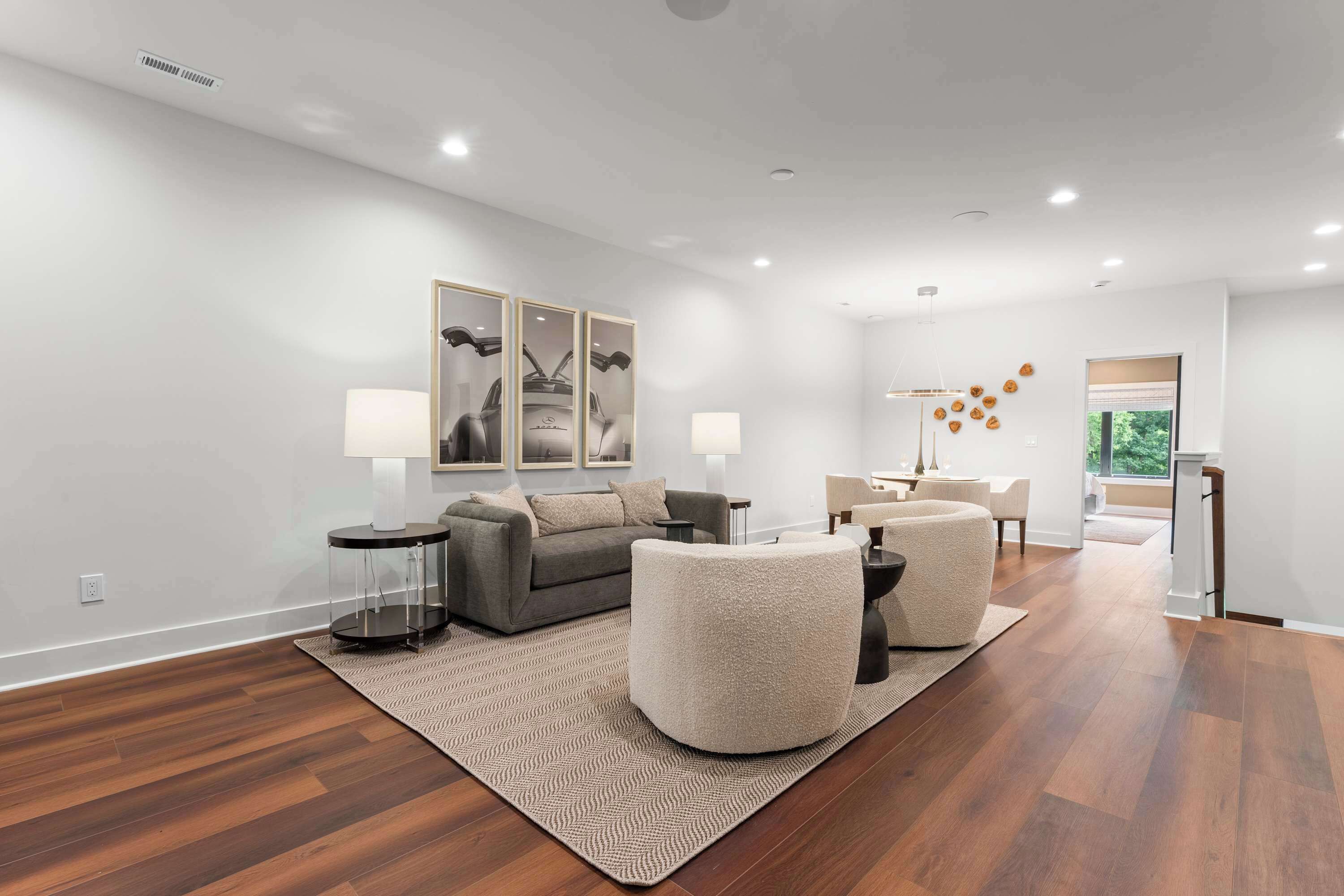 A modern living room with a grey sofa, round ottoman, and a coffee table. There is a rug on the floor, a lamp, and a painting on the wall.