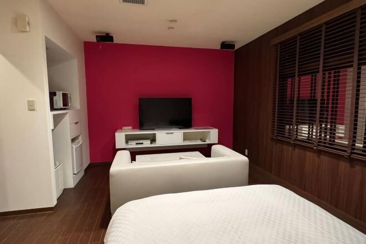 A hotel room with a bed, a television, a white desk, and a red wall.