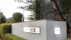 Segnaletica di un hotel con il nome 'Luxe' e una piccola targa con il numero '1111' su una parete grigia.