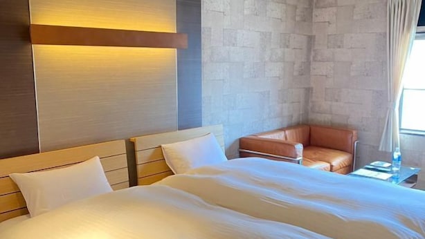 Camera d'albergo con un letto grande, una poltrona in pelle, un comodino e una lampada a parete.