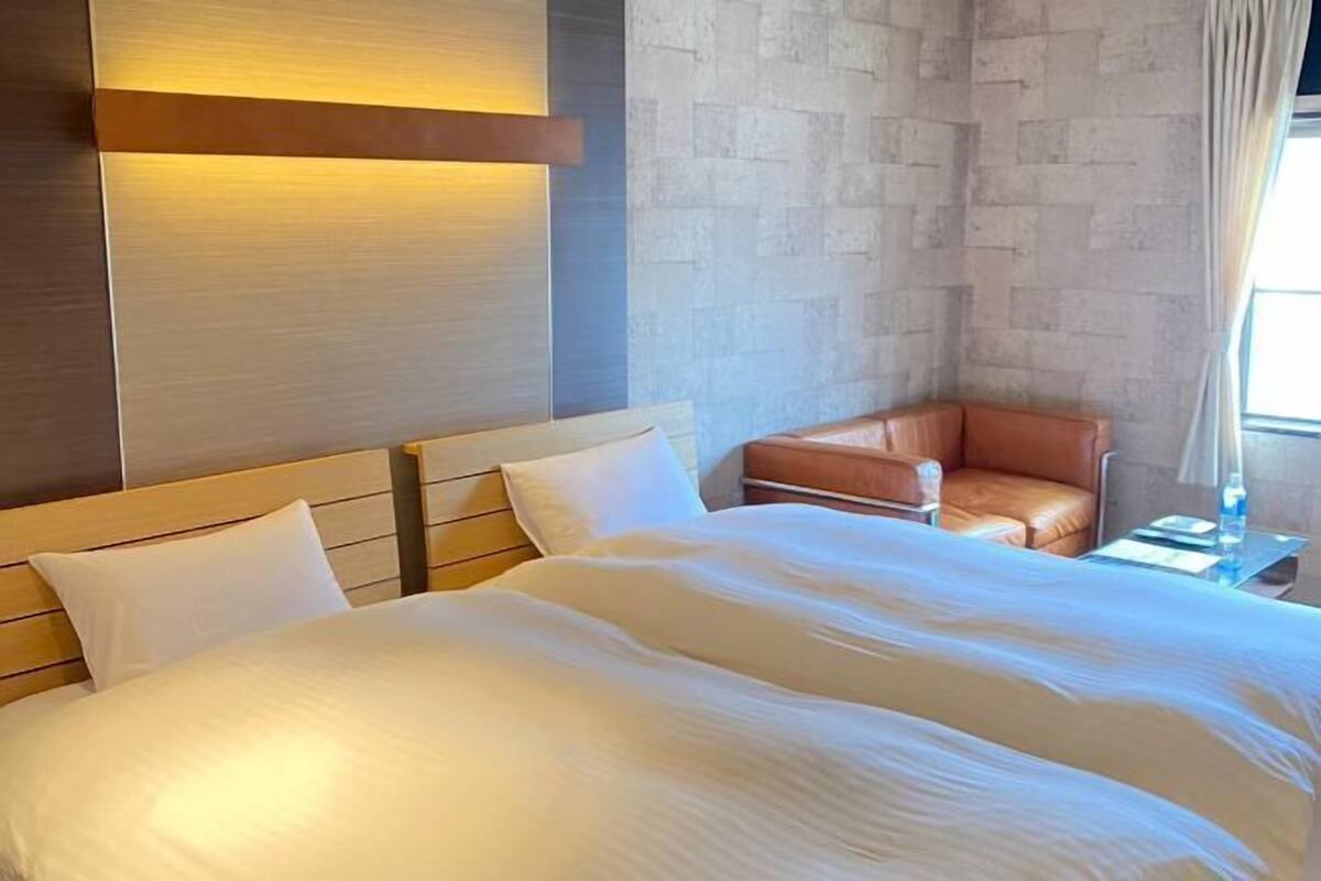 A hotel room with a large bed, a leather armchair, a nightstand, and a wall-mounted light.