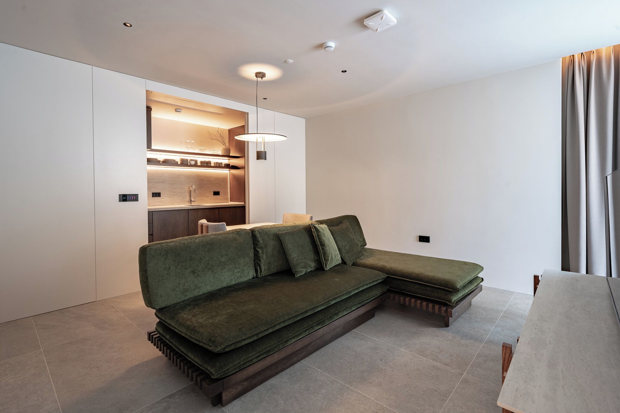 A modern living room with a sectional sofa, built-in shelving, pendant lighting, and a dining area.