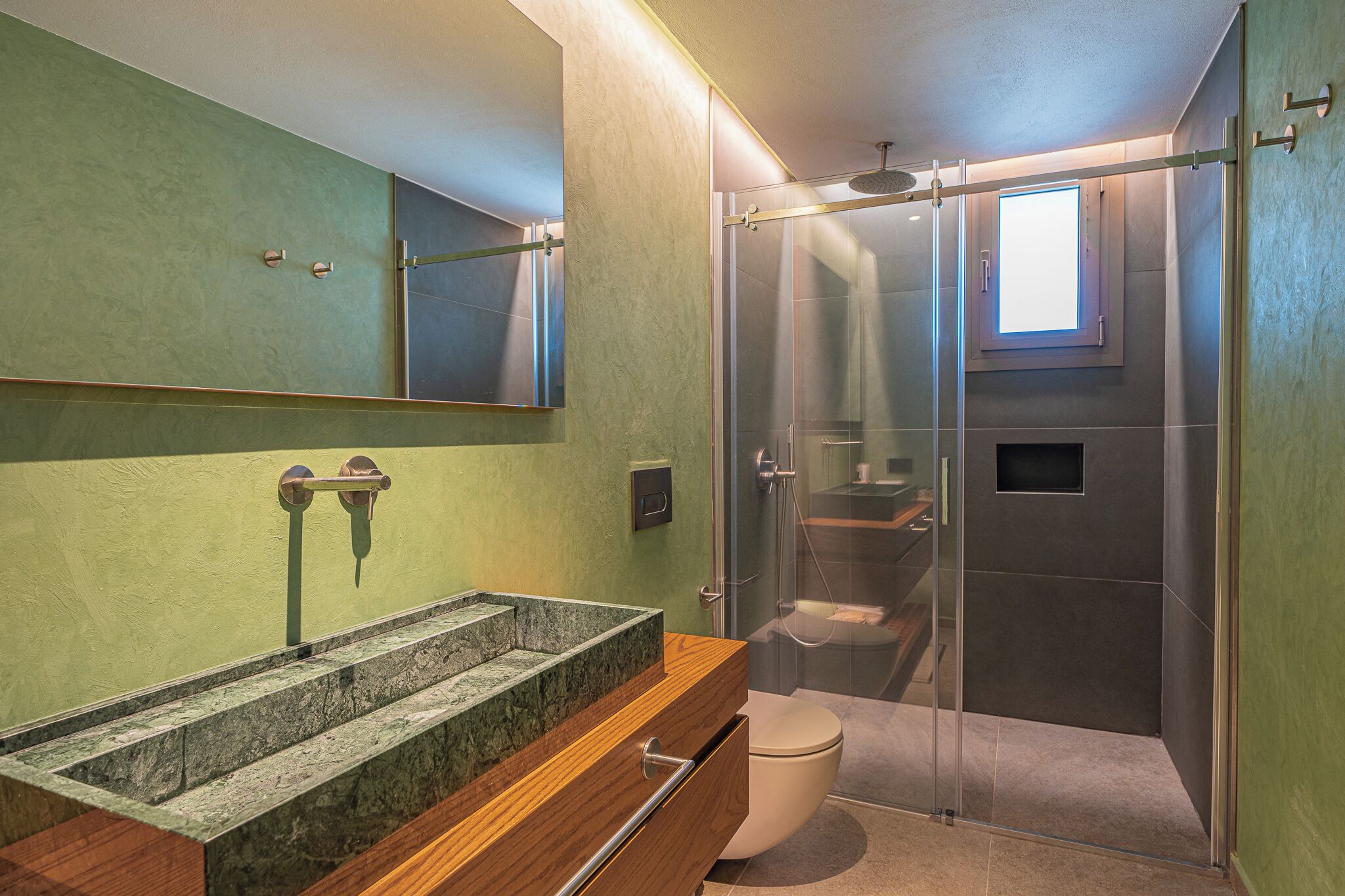 Un baño moderno con ducha envuelta en vidrio, lavamanos de mármol y retrete.