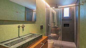 Un baño moderno con ducha envuelta en vidrio, lavamanos de mármol y retrete.