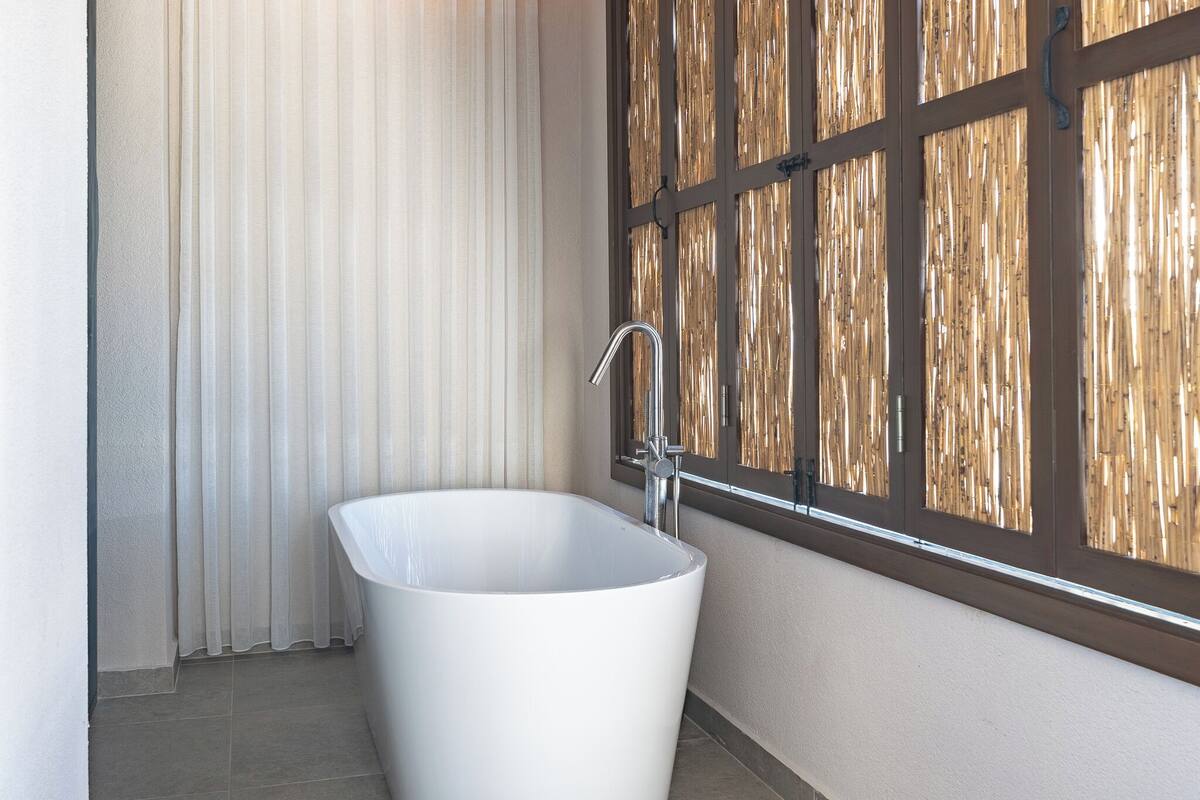 Une salle de bain moderne avec une baignoire sur pieds, une fenêtre avec des stores en bambou et un sol carrelé.