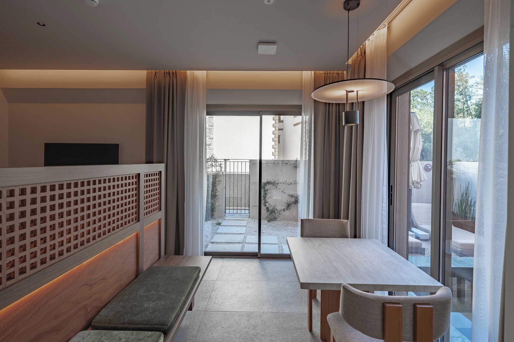 A modern hotel room with a balcony, a dining area, and a TV.