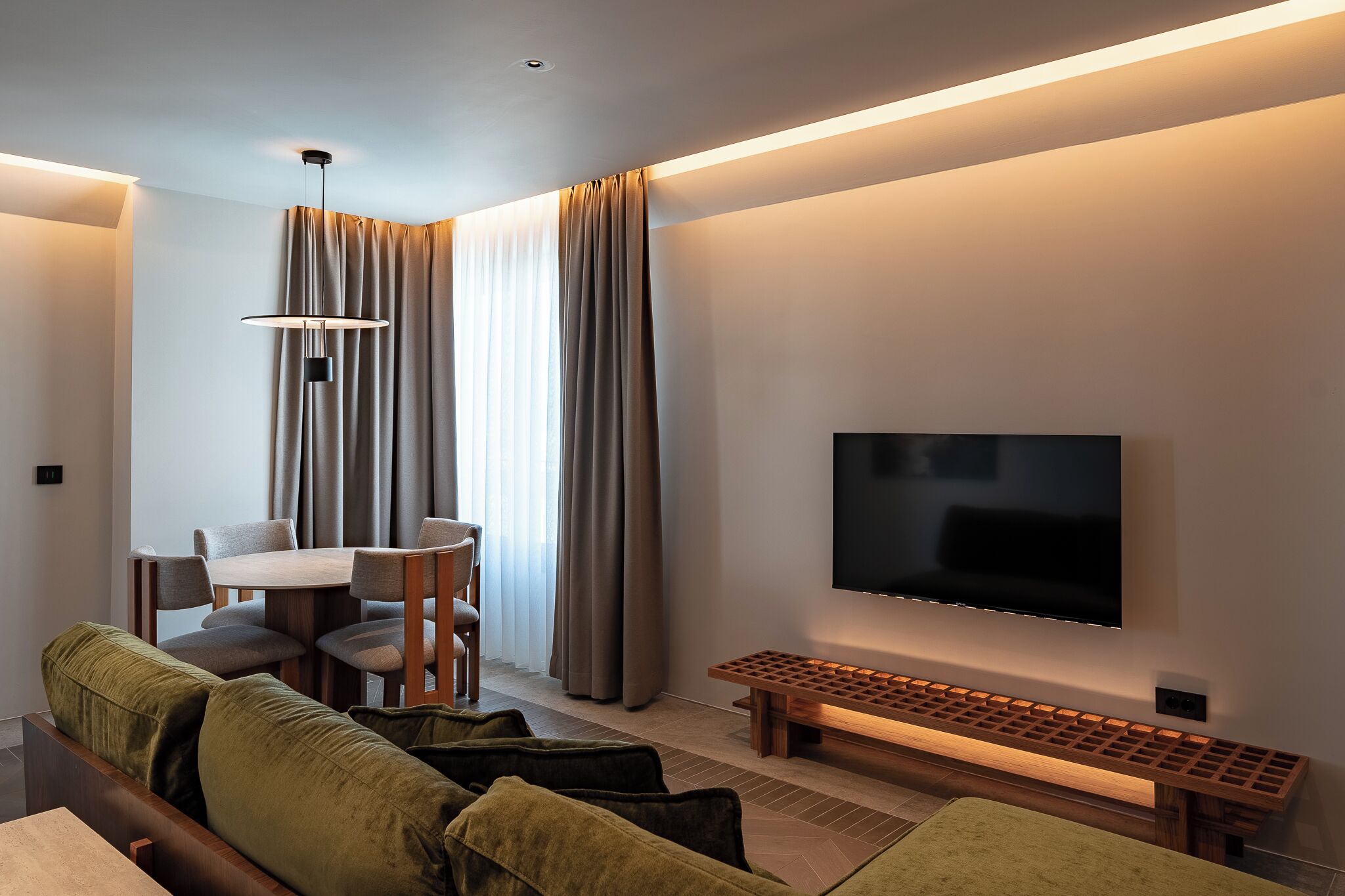 Una sala de estar moderna con un televisor de pantalla plana, un banco de madera, una mesa de comedor con sillas y un sofá.