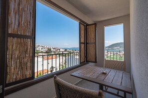 Un balcon donnant sur une vue panoramique de la ville, une table en bois et une chaise en osier.