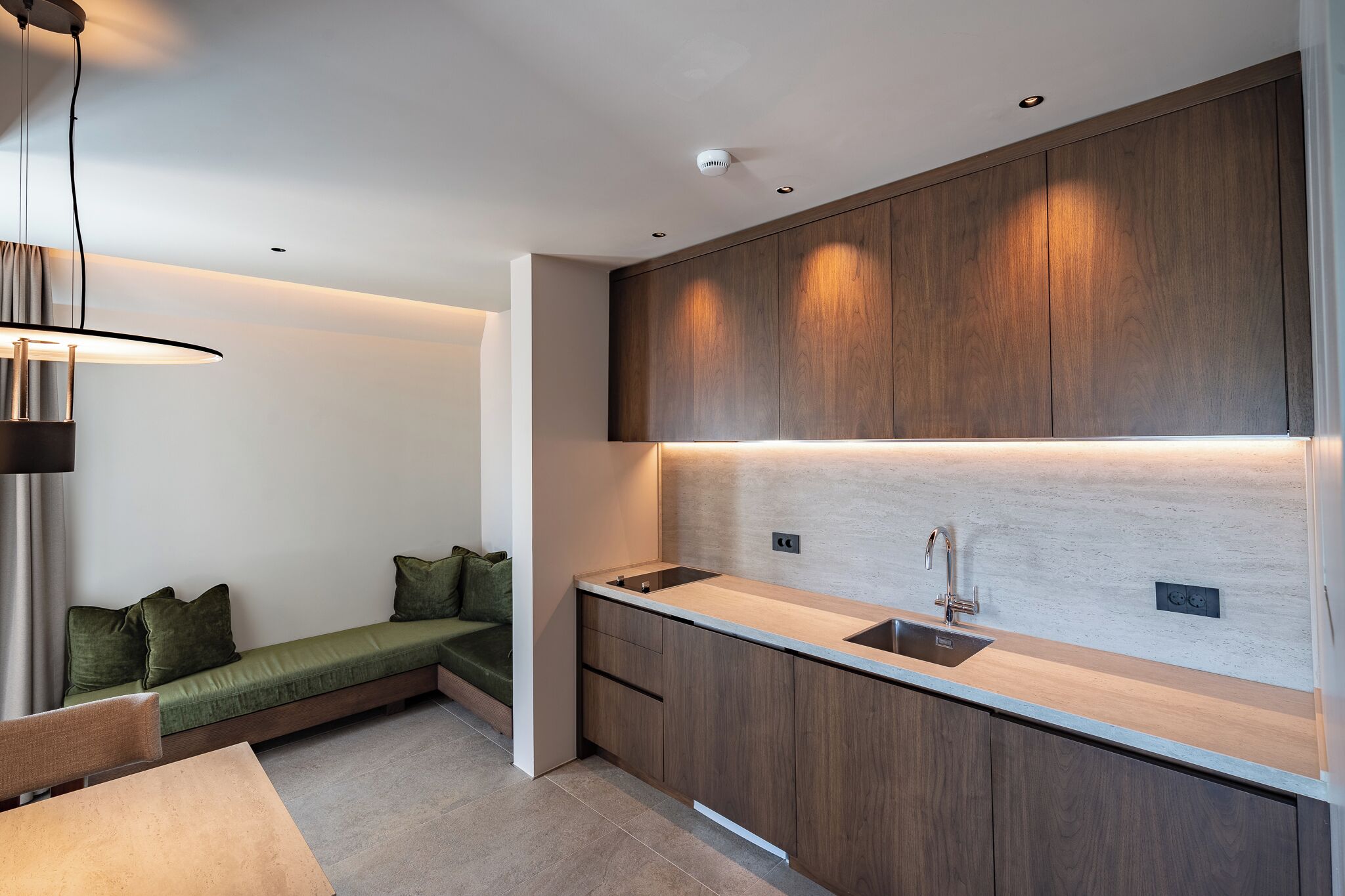 A modern kitchen with wooden cabinets, a built-in sink, and a bench with cushions.