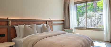 Une chambre d’hôtel avec un grand lit, une table de chevet, une fenêtre avec des rideaux et une vue sur la verdure.