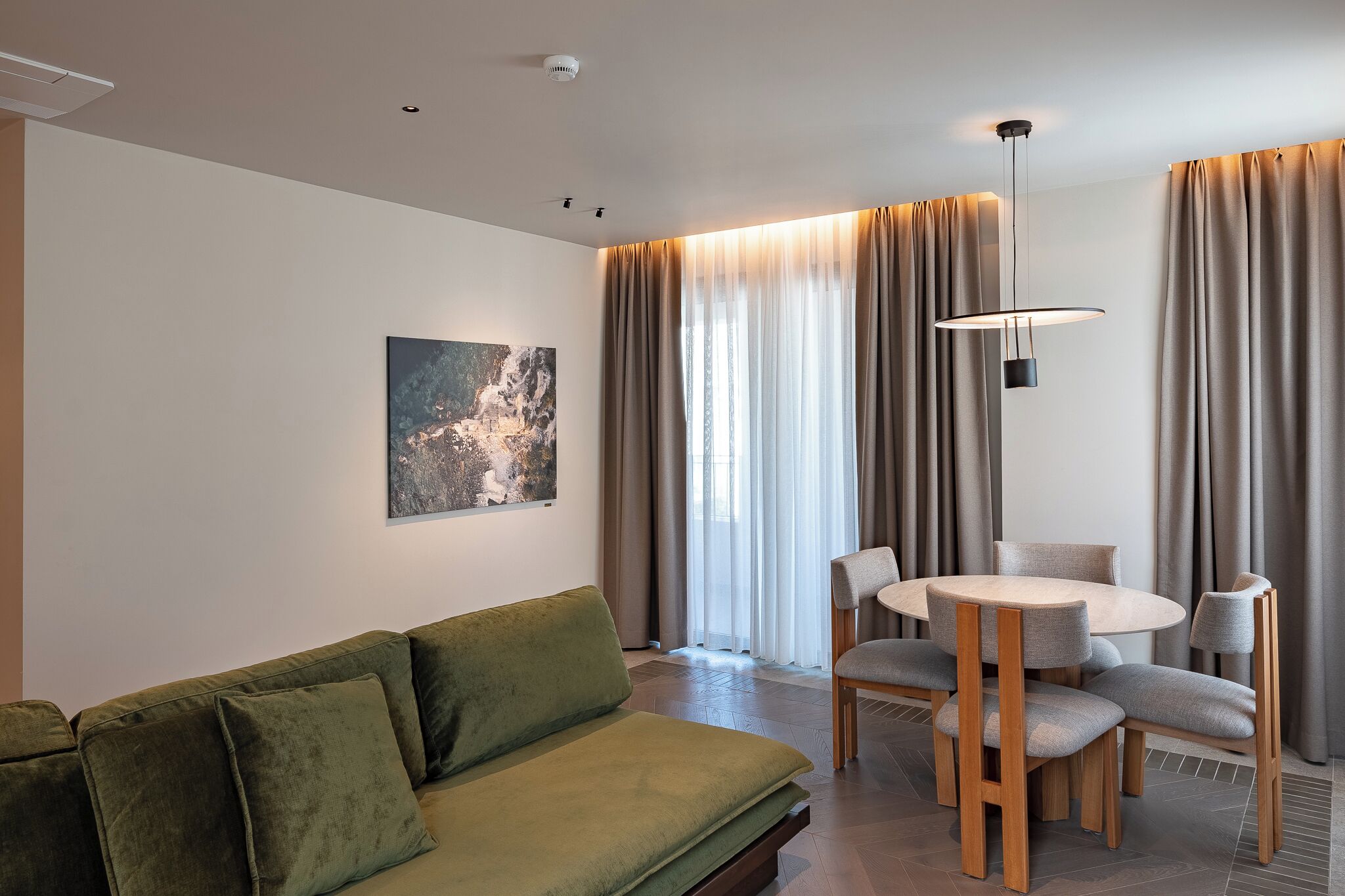 Ein modernes Wohnzimmer mit einem grünen Sofa, einem runden Esstisch mit Stühlen, einer Pendelleuchte und einem Bild an der Wand.