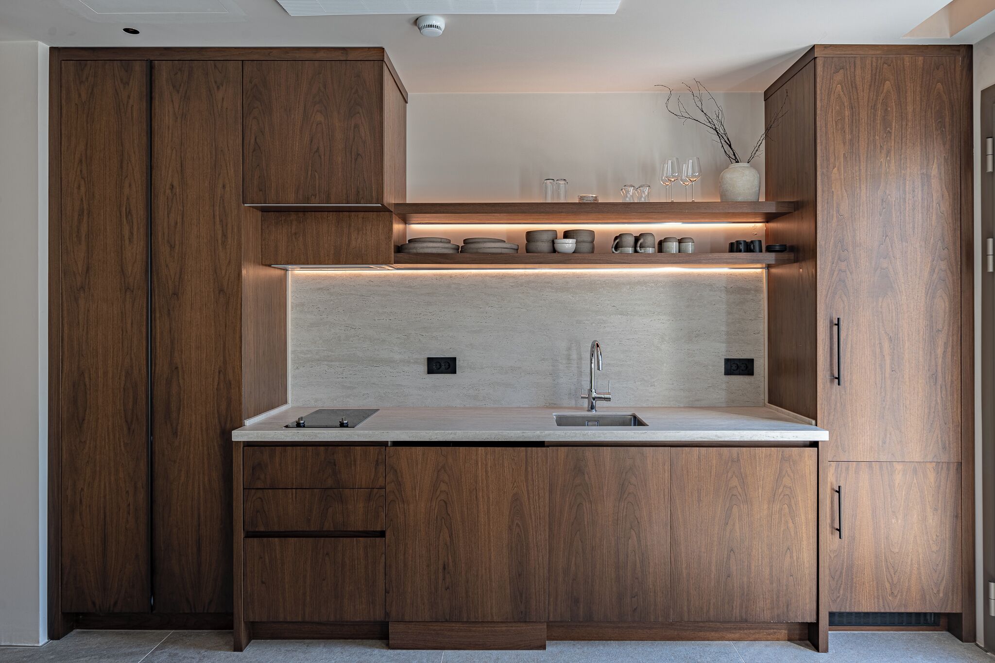 A modern kitchen with wooden cabinets, a countertop, a sink, and a built-in shelf with glassware.