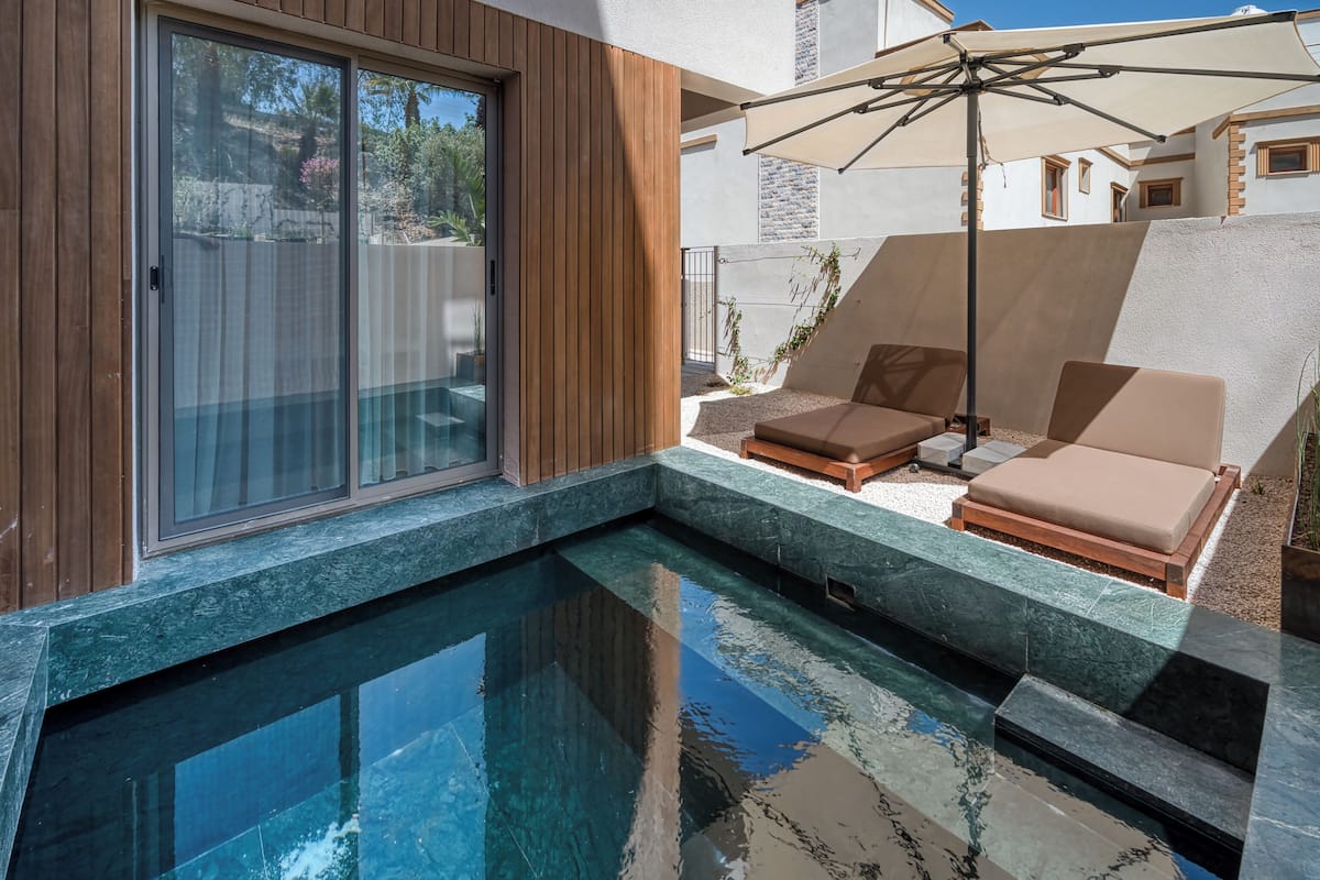 Un espace piscine extérieur moderne, doté d’une porte vitrée, de chaises longues et d’un parasol.