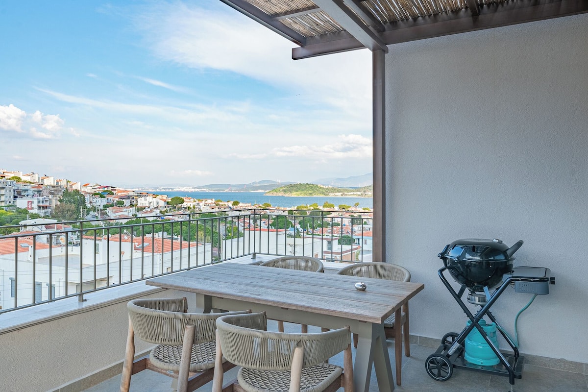 Un balcon avec une table et des chaises, un barbecue et une vue sur une ville côtière.