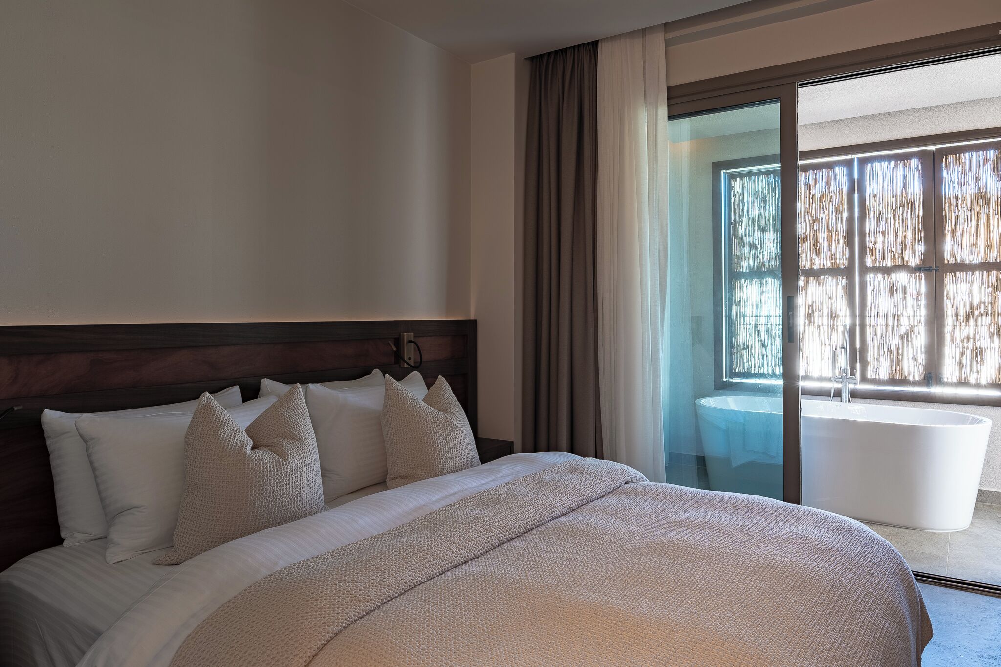 A hotel room with a large bed, a view of a bathtub, and a sliding glass door to a balcony.