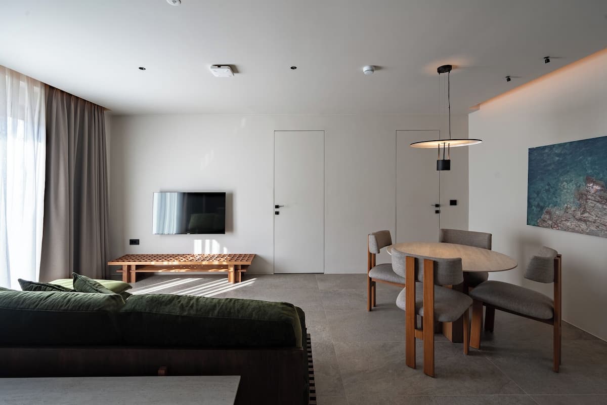 Une chambre d’hôtel moderne, équipée d’un lit, d’une télévision, d’une table à manger avec des chaises et d’un tableau au mur.