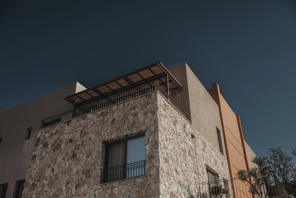 Un immeuble doté d’une façade en pierre, d’un balcon avec des balustrades en métal et d’une fenêtre ornée d’un rideau.